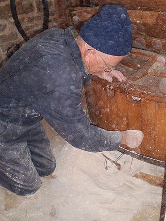 Roland Tetrault clears the freshly ground flour from the stones.  The round specs in the photo are from the flash reflecting off flour dust in the air.