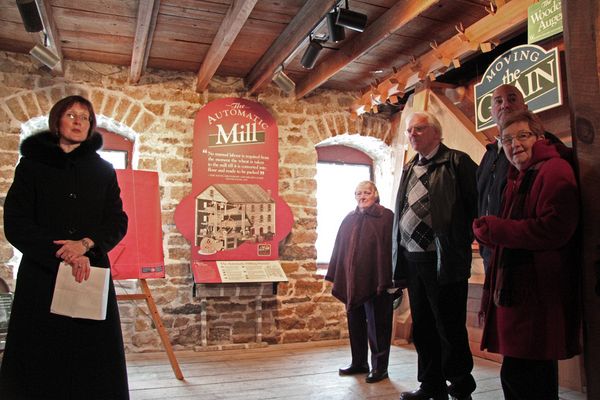Natalie Bolton, Director, Mail Operations for Canada Post explains why the Old Stone Mill was chosen for the stamp.  On the right, Mary Freiday (director, DMS), Ron Holman, Art Cowan (President, DMS) and Anna Greenhorn (director, DMS) look on