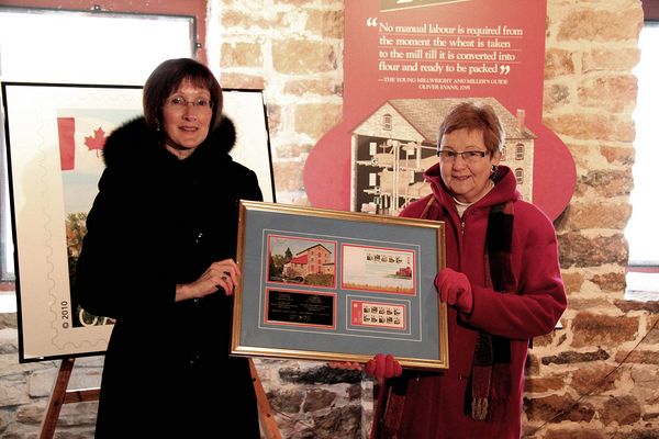 Natalie Bolton, Director, Mail Operations, Canada Post (left) and Anna Greenhorn, Director, Delta Mill Society hold a commemorative plaque showing the stamps.