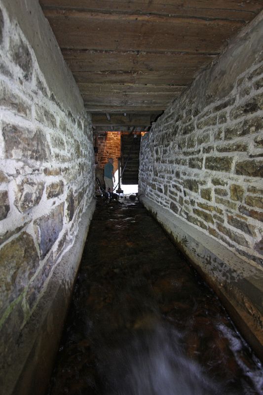 In the millrace, looking south, downstream towards the waterwheel.  One of the mysteries of the mill is why the raceway isn't parallel to the waterwheel.  In part because our replica waterwheel may be closer to the west wall than the original wheel, which may have been positioned a couple of feet to the east.  It also supports the idea that a wooden sluide was used, correcting the angle of the raceway.